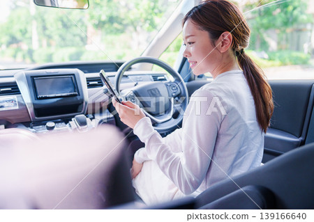 A woman passing the time in the driver's seat of a car. 139166640