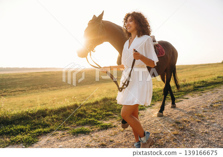 The walk on the footpath. Woman in white dress is with horse on the countryside field The walk on the footpath. Woman in white dress is with horse on the countryside field 139166675