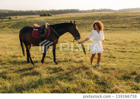 Warm season, farming conception. Woman in white dress is with horse on the countryside field 139166738