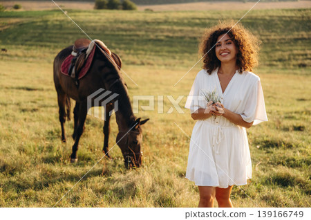 Grass is in hands. Woman in white dress is with horse on the countryside field Grass is in hands. Woman in white dress is with horse on the countryside field 139166749