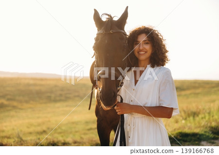 Against the horizon background. Woman in white dress is with horse on the countryside field Against the horizon background. Woman in white dress is with horse on the countryside field 139166768