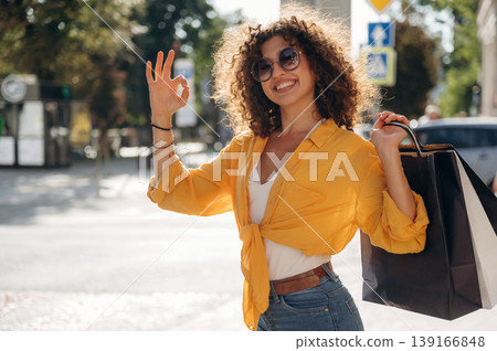 Sunny weather, having a walk. Happy woman is with shopping bags in town Sunny weather, having a walk. Happy woman is with shopping bags in town 139166848