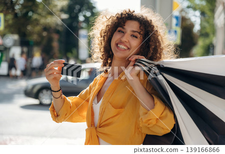 Credit card is in hand. Happy woman is with shopping bags in town Credit card is in hand. Happy woman is with shopping bags in town 139166866