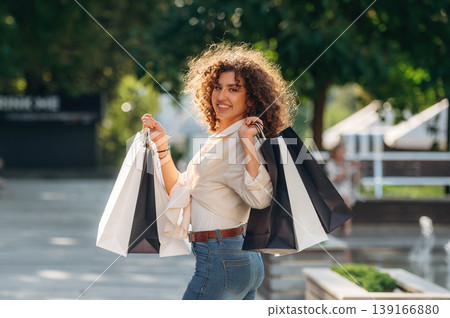 Brown curly hair. Happy woman is with shopping bags in town Brown curly hair. Happy woman is with shopping bags in town 139166880