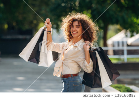 Brown curly hair. Happy woman is with shopping bags in town Brown curly hair. Happy woman is with shopping bags in town 139166882