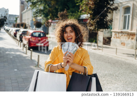 Bunch of money in hands. Happy woman is with shopping bags in town 139166913