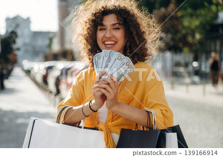 Bunch of money in hands. Happy woman is with shopping bags in town Bunch of money in hands. Happy woman is with shopping bags in town 139166914