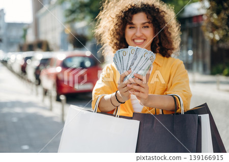 Lot of money. Happy woman is with shopping bags in town Lot of money. Happy woman is with shopping bags in town 139166915
