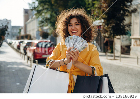 Bunch of money in hands. Happy woman is with shopping bags in town Bunch of money in hands. Happy woman is with shopping bags in town 139166929