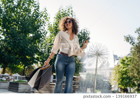 With smartphone. Happy woman is with shopping bags in town With smartphone. Happy woman is with shopping bags in town 139166937