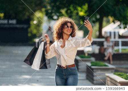 Phone is in hand. Happy woman is with shopping bags in town 139166943