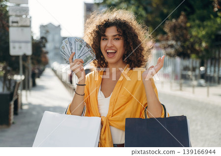 Sincere smile, holding lot of money. Happy woman is with shopping bags in town Sincere smile, holding lot of money. Happy woman is with shopping bags in town 139166944