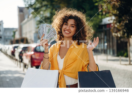 Sincere smile, holding lot of money. Happy woman is with shopping bags in town Sincere smile, holding lot of money. Happy woman is with shopping bags in town 139166946