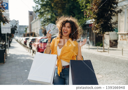 Sincere smile, holding lot of money. Happy woman is with shopping bags in town Sincere smile, holding lot of money. Happy woman is with shopping bags in town 139166948