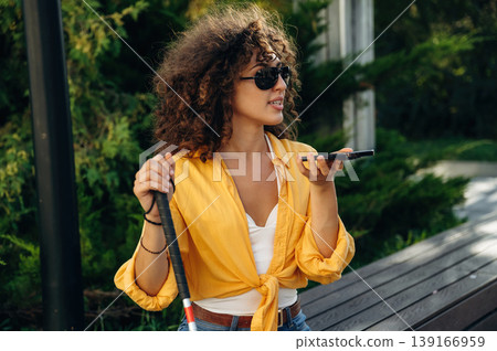 Talking by phone. A blind woman is in the modern city at daytime Talking by phone. A blind woman is in the modern city at daytime 139166959