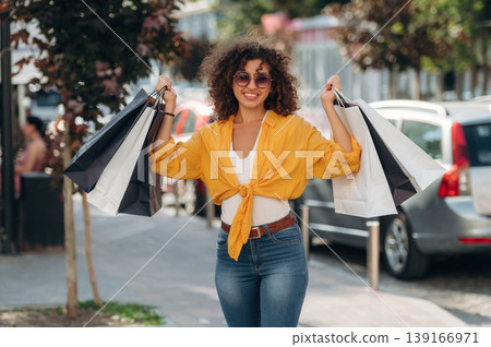 In blue jeans. Happy woman is with shopping bags in town In blue jeans. Happy woman is with shopping bags in town 139166971
