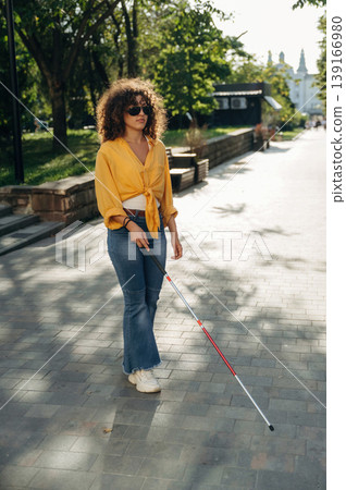 Using white cane. A blind woman is in the modern city at daytime Using white cane. A blind woman is in the modern city at daytime 139166980