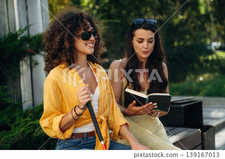 Woman is reading the book for a blind person, sitting outdoors in the public park Woman is reading the book for a blind person, sitting outdoors in the public park 139167013