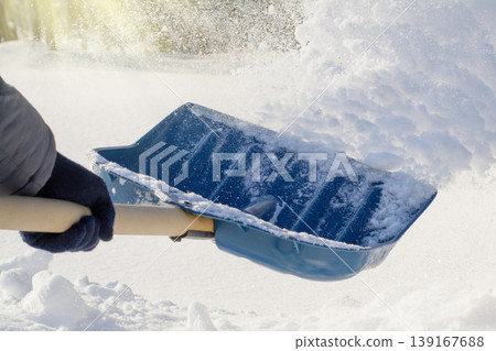 Young man cleaning snow after a blizzard in a sunny morning in winter. Throwing snow while cleaning 139167688
