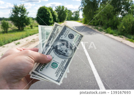 Dollar bills in male hand against a new asphalt road 139167693