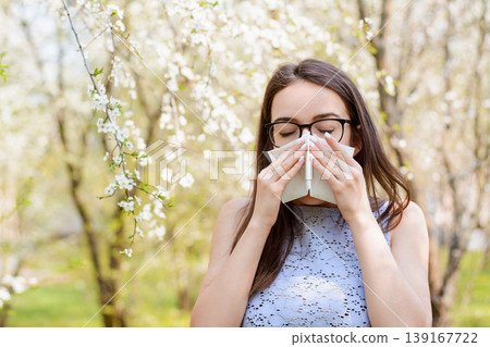 Young female with long natural hair in light blouse sneezing because of bloom pollen from trees in spring. Concept of allergy on pollen 139167722