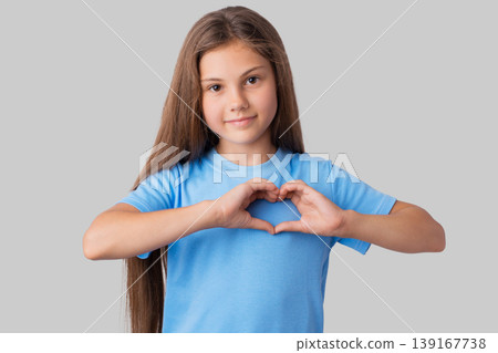 Adorable small girl in blue t-shirt making a heart gesture with her fingers with a happy sincere smile. Studio portrait of a little beautiful girl showing heart with her hands 139167738