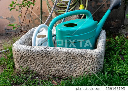 watering cans at a garden tap next to a concrete wall 139168195