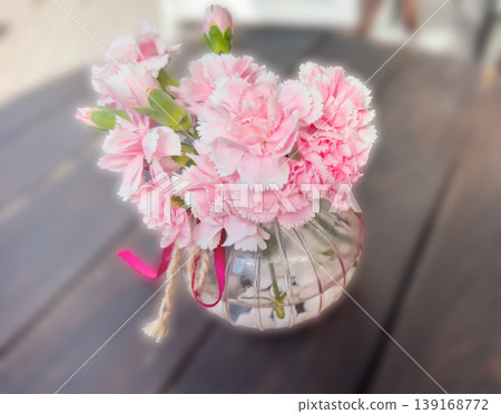 Pink carnations bouquet in vase with flowers floral arrangement on table, decor for romantic home styling. Soft pastel petals, glass vessel and ribbon create an elegant still life. Pink carnations bouquet in vase with flowers floral arrangement on table, decor for romantic home styling. Soft pastel petals, glass vessel and ribbon create an elegant still life. 139168772