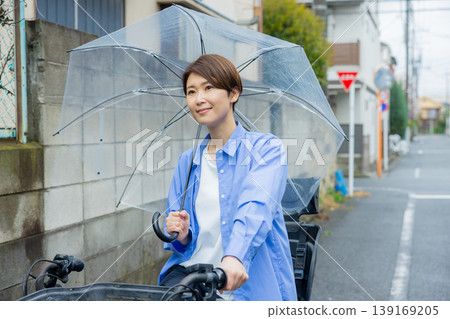 一名女子騎著腳踏車,手裡拿著一把傘。 一名女子騎著腳踏車,手裡拿著一把傘。 139169205