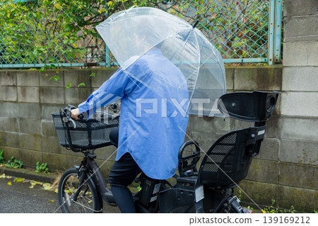 A woman riding a bicycle while holding an umbrella. A woman riding a bicycle while holding an umbrella. 139169212
