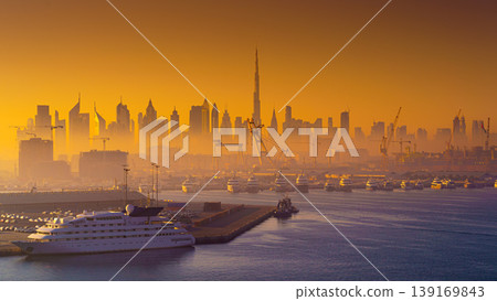 Dubai, United Arab Emirates - Jan 12 2024, Panoramic view of downtown Dubai skyscrapers, with Burj Khalifa, at dawn in a haze, with port and ship on foreground, Dubai, United Arab Emirates Dubai, United Arab Emirates - Jan 12 2024, Panoramic view of downtown Dubai skyscrapers, with Burj Khalifa, at dawn in a haze, with port and ship on foreground, Dubai, United Arab Emirates 139169843