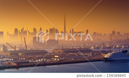 Dubai, United Arab Emirates - Jan 12 2024, Panoramic view of downtown Dubai skyscrapers, with Burj Khalifa, at dawn in a haze, with port and ship on foreground, Dubai, United Arab Emirates Dubai, United Arab Emirates - Jan 12 2024, Panoramic view of downtown Dubai skyscrapers, with Burj Khalifa, at dawn in a haze, with port and ship on foreground, Dubai, United Arab Emirates 139169845