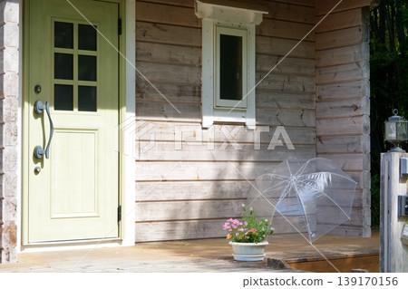 Potted flowers and a plastic umbrella drying outside the entrance of a log house. 139170156