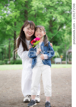 母親節當天，一位母親和女兒面帶微笑地看著鏡頭，手捧康乃馨，背景是新鮮的綠植，照片配文是“謝謝你的一切！”（全身照，豎圖） 139171598