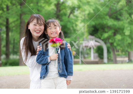 母親節這天，一對母女面帶微笑，手捧康乃馨，在綠意盎然的背景下對著鏡頭說：“媽媽，謝謝你的一切！” 139171599