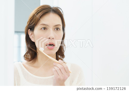 A middle-aged Japanese woman brushing her teeth in the mirror. 139172126