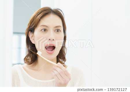 A middle-aged Japanese woman brushing her teeth in the mirror. 139172127