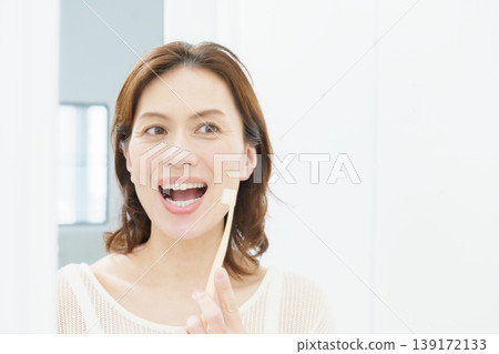 A middle-aged Japanese woman brushing her teeth in the mirror. 139172133