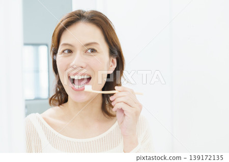A middle-aged Japanese woman brushing her teeth in the mirror. 139172135