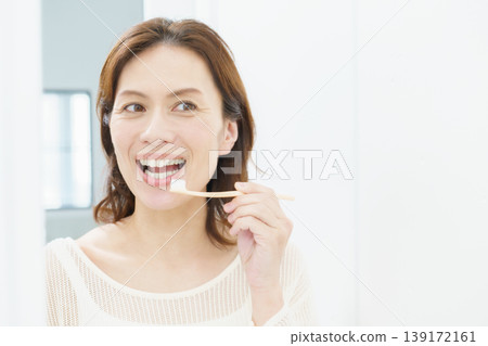 A middle-aged Japanese woman brushing her teeth in the mirror. 139172161