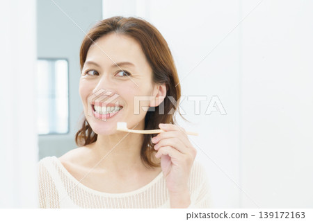 A middle-aged Japanese woman brushing her teeth in the mirror. 139172163