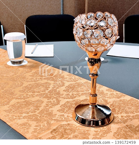 elegant photo of round table is covered with a gray tablecloth with gold decoration and a beautiful vase is placed in the middle and there is a clear glass filled with mineral water. elegant photo of round table is covered with a gray tablecloth with gold decoration and a beautiful vase is placed in the middle and there is a clear glass filled with mineral water. 139172459