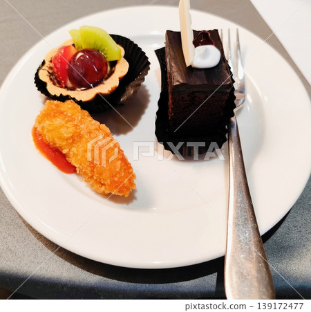 dessert in the form of chocolate cup cake, pieces of strawberry, annona squamosa and grapes and fried teoung rolls containing chicken served on a ceramic plate with a fork on the table dessert in the form of chocolate cup cake, pieces of strawberry, annona squamosa and grapes and fried teoung rolls containing chicken served on a ceramic plate with a fork on the table 139172477