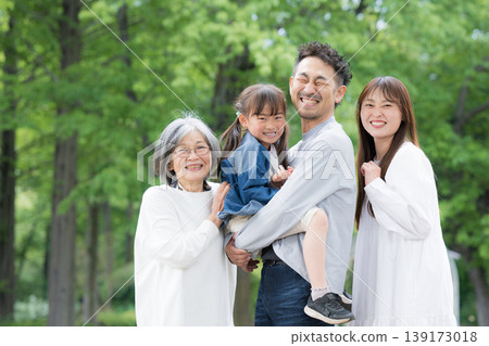 A three-generation family's smiling, camera-facing portrait; a close-up of their upper bodies capturing their happy family life in a park surrounded by fresh greenery. A three-generation family's smiling, camera-facing portrait; a close-up of their upper bodies capturing their happy family life in a park surrounded by fresh greenery. 139173018