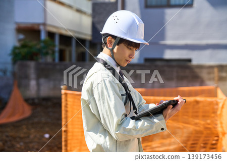A male site supervisor is holding a tablet to check the status of the construction site. A male site supervisor is holding a tablet to check the status of the construction site. 139173456