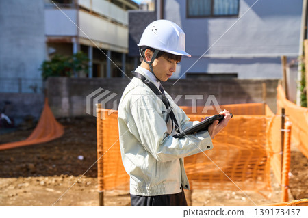 A male site supervisor is holding a tablet to check the status of the construction site. A male site supervisor is holding a tablet to check the status of the construction site. 139173457