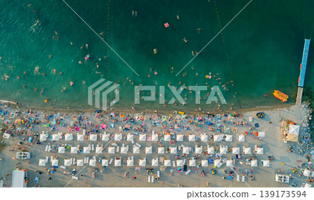 Aerial view of a vibrant beach filled with bathers enjoying warm water and sun under white umbrellas Aerial view of a vibrant beach filled with bathers enjoying warm water and sun under white umbrellas 139173594