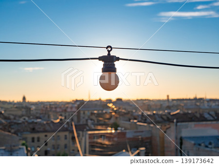 Warm glow of a setting sun highlighting a lone light bulb above a sprawling urban landscape Warm glow of a setting sun highlighting a lone light bulb above a sprawling urban landscape 139173642