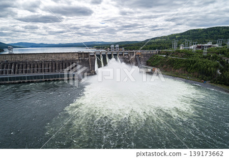 Aerial view of concrete dam releasing water into river on cloudy day. Water discharge at hydroelectric power plant. 139173662