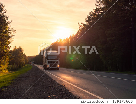 Large commercial truck travels along the highway surrounded by dense pine forest at sunset 139173666